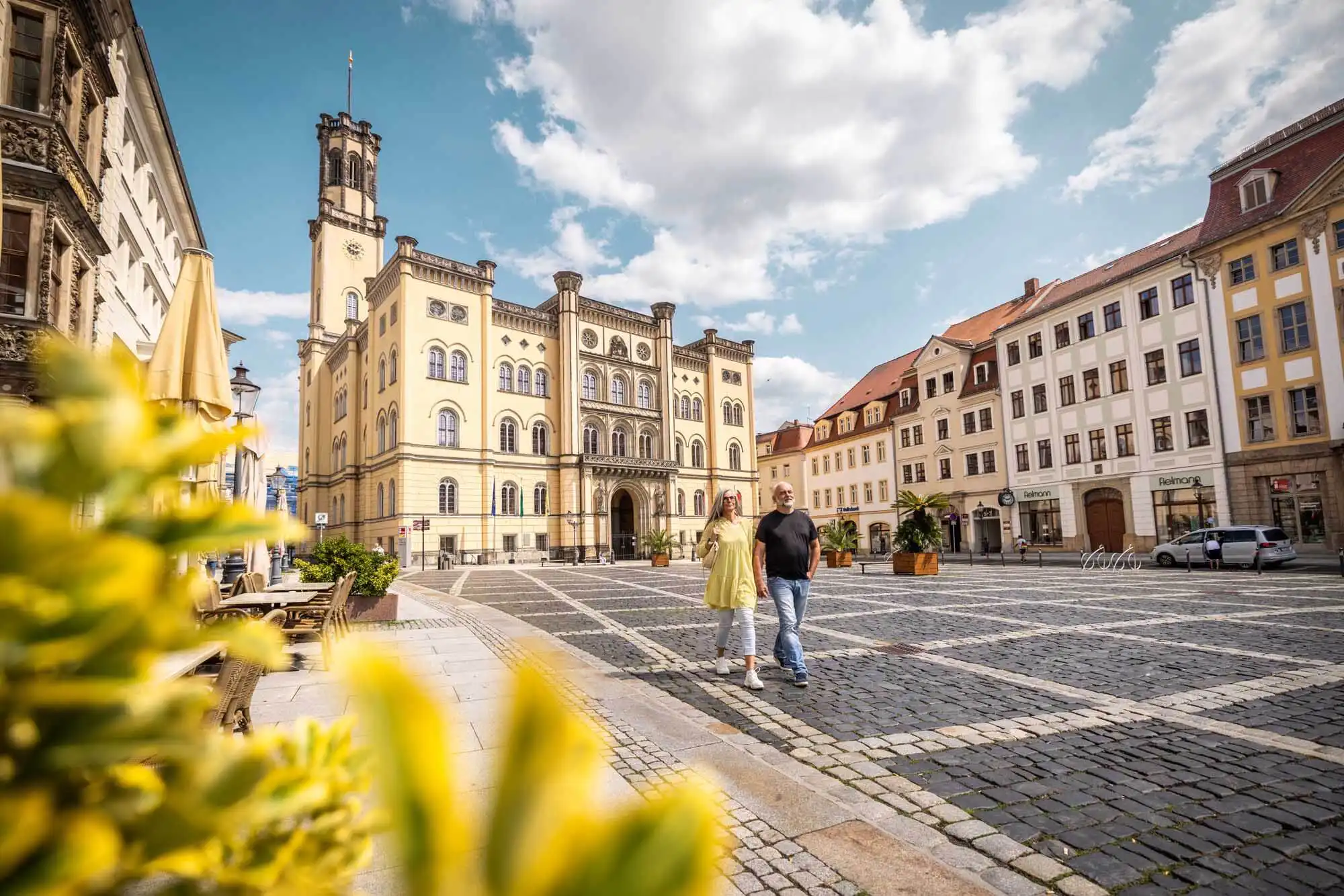 Marktplatz von Zittau. Im Hintergrund das Rathaus. Zwei Personen schlendern über den Marktplatz.